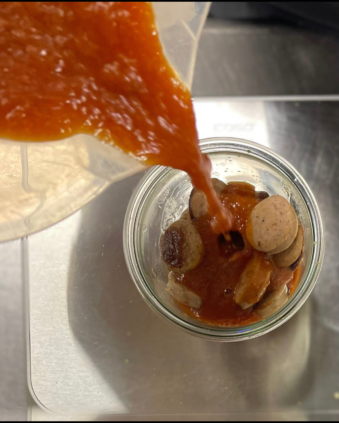 Hier sieht man den Herstellungsprozess der BierCurrywurst im Glas. Die geschnittene Wurst befindet sich im Glas und es wird gerade der Curryketchup eingefüllt.