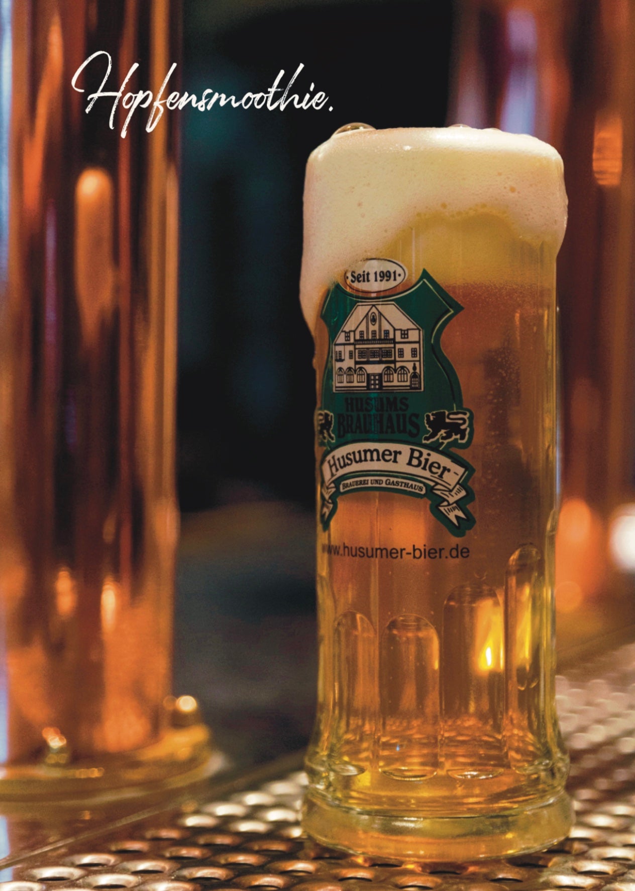 Auf dem Foto sieht man ein 0,5 l gezapftes Husumer Hell im Bierseidel. Oben auf dem Bild steht "Hopfensmoothie."