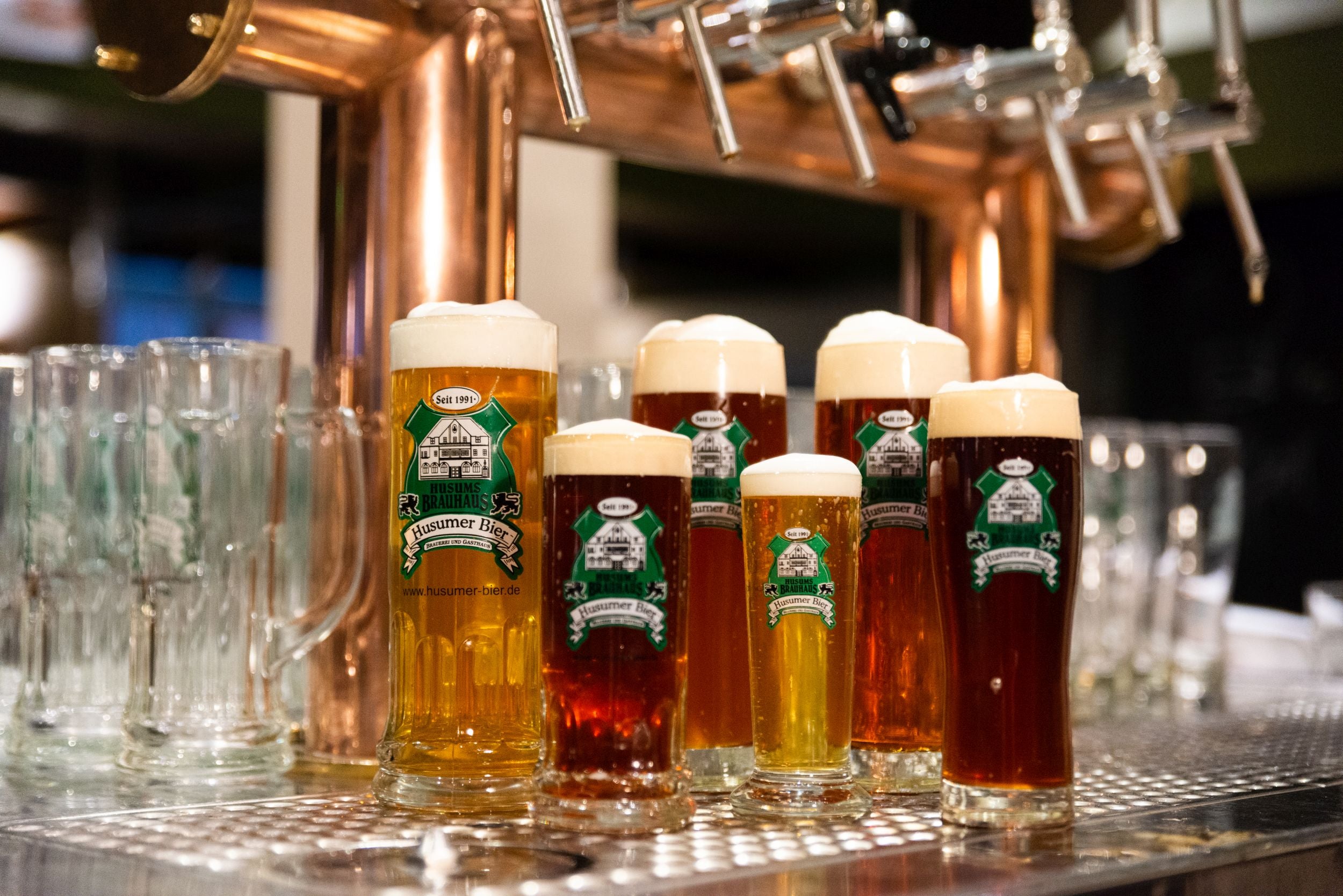 Auf dem Foto sieht man mehre gezapfte Biere mit Schaumkrone vor dem Zapfhahn stehen.